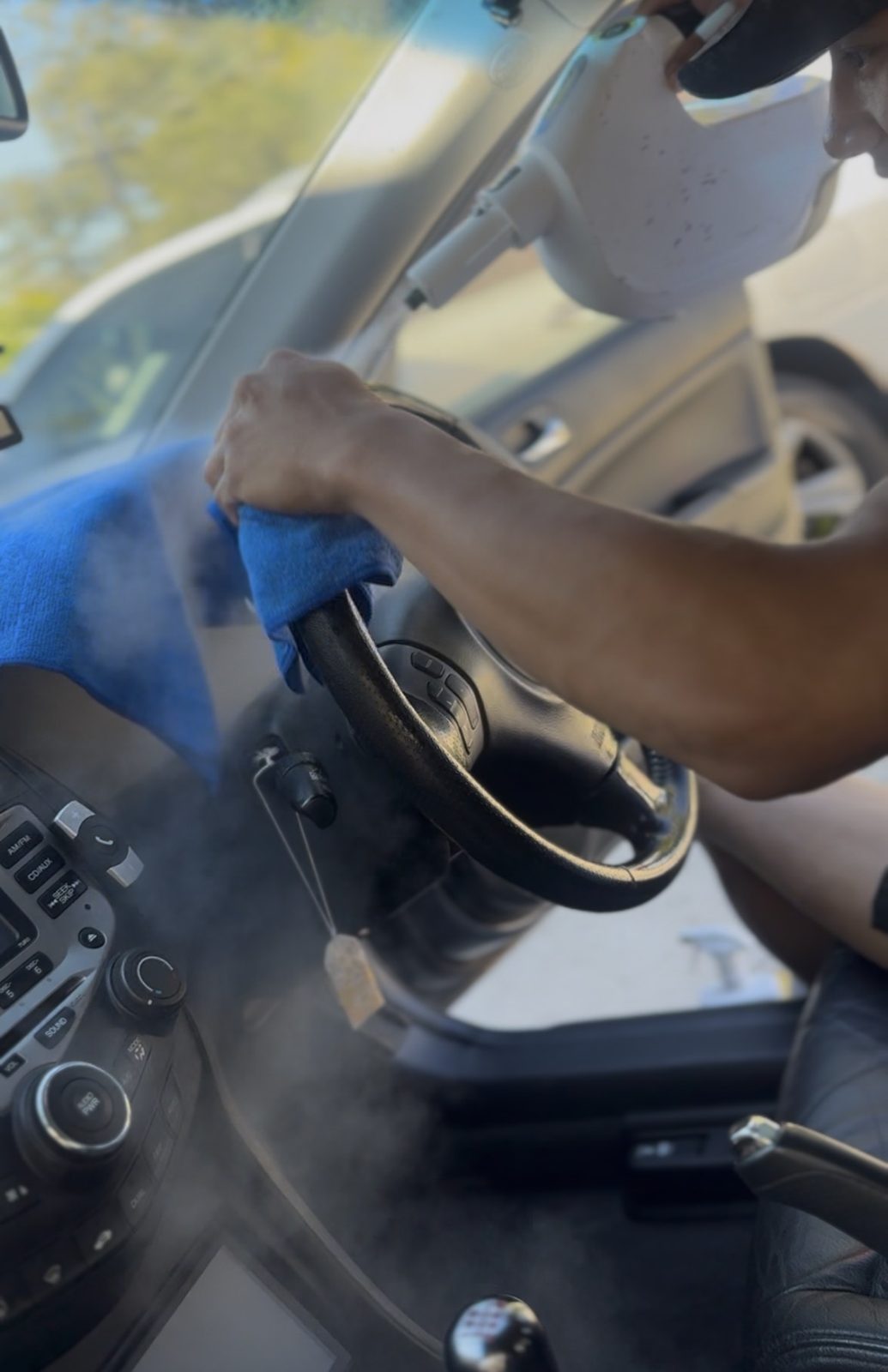 Detailer steam cleaning a steering wheel with a blue microfibre towel